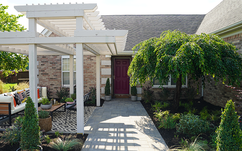 white pergola with pink door and weeping tree and boxwoods in cone topiaries