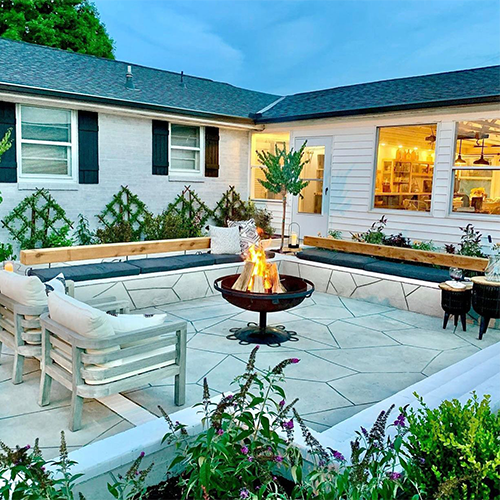 white house with black shutters and green pyracantha espeliares in background, fire pit in center and pruple buddleja flowers in foreground at bottom
