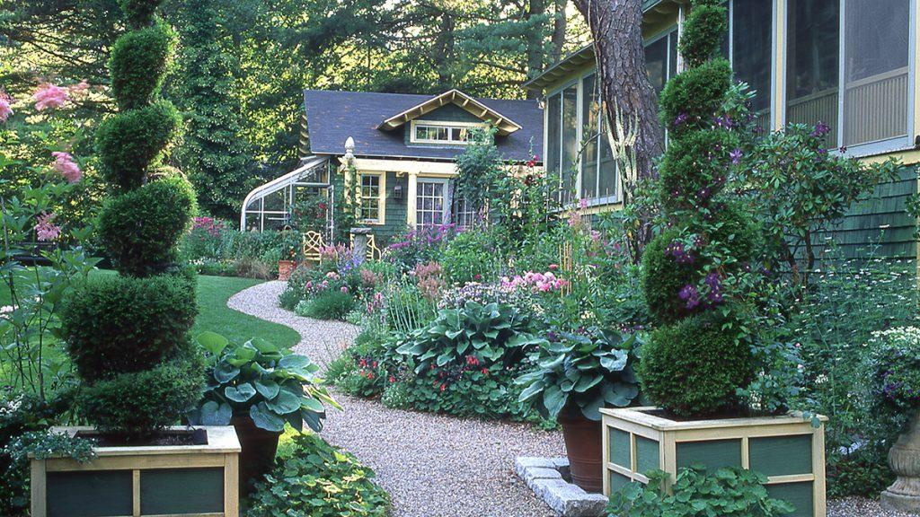 Cottage garden scene with a path filled with green shrubs and different colored flowers. 