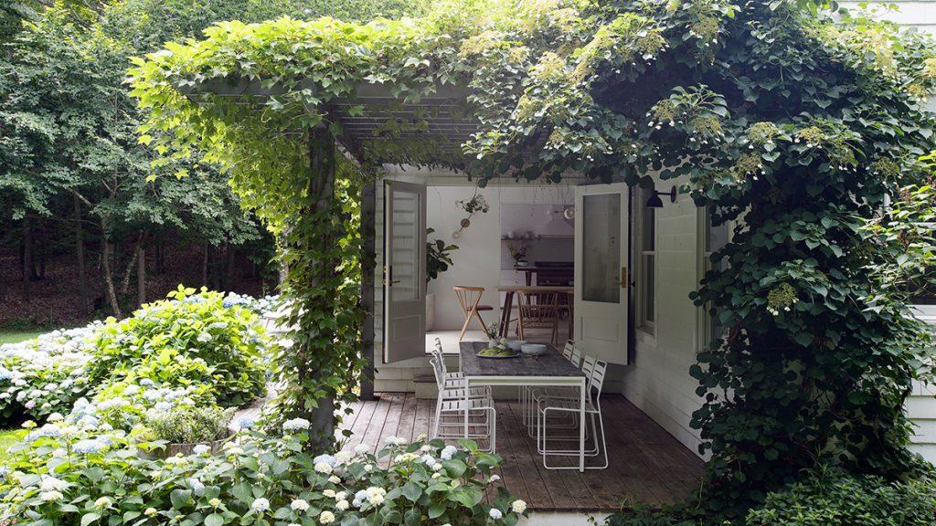 All white nook-sized dining space completely covered in vining plants on the roof and sides featuring a table in the center.