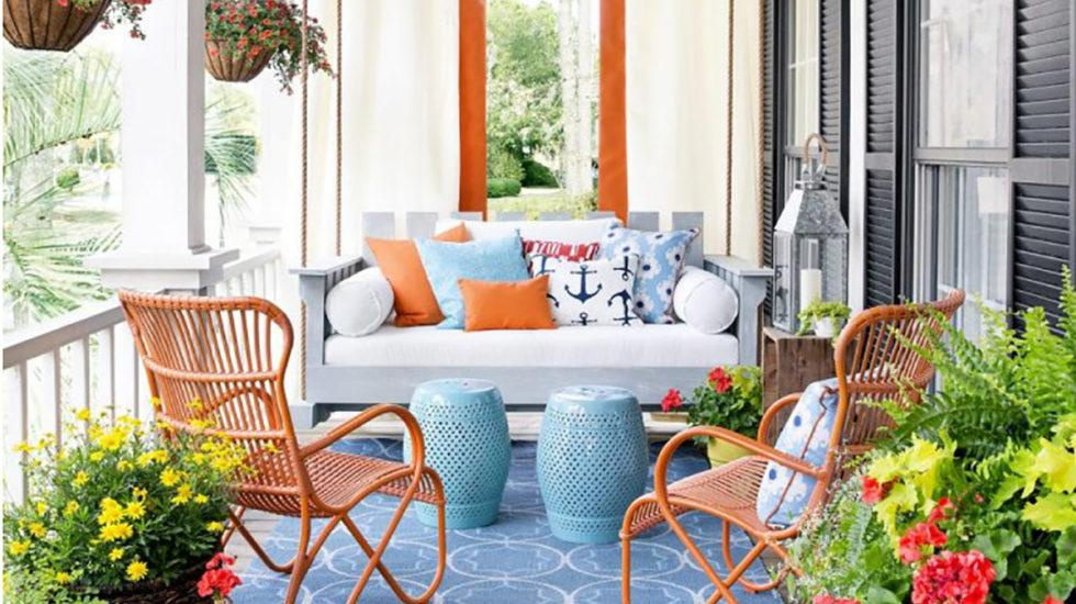 Porch with a couch, chairs, pillows, and hanging flower baskets, potted yellow flowers, and potted pink flowers with ferns.