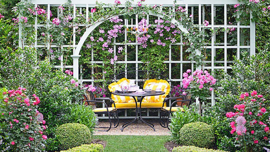 Patio table with an archway and wall of flowers as well as boxwood and other evergreen shrubs.