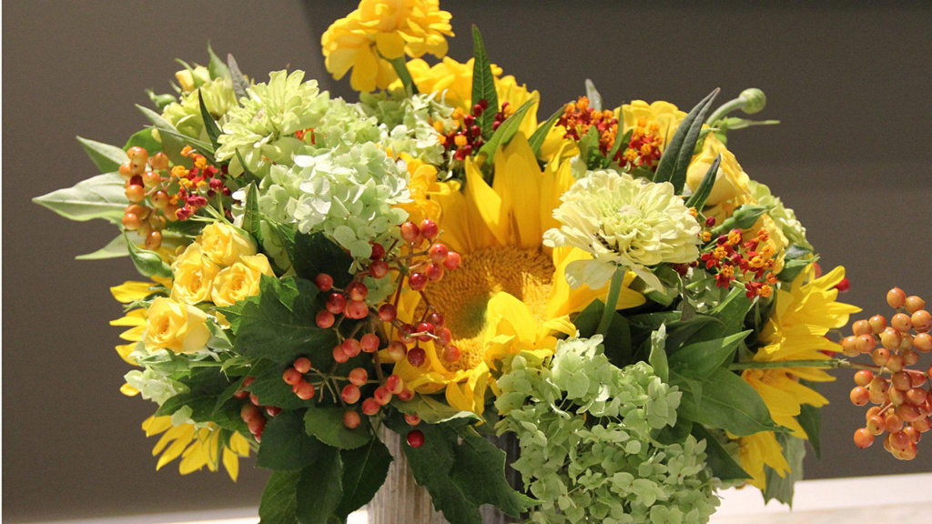 Flower arrangement filled with sunflowers, hydrangeas, roses, zinnias, and berries in a vase.