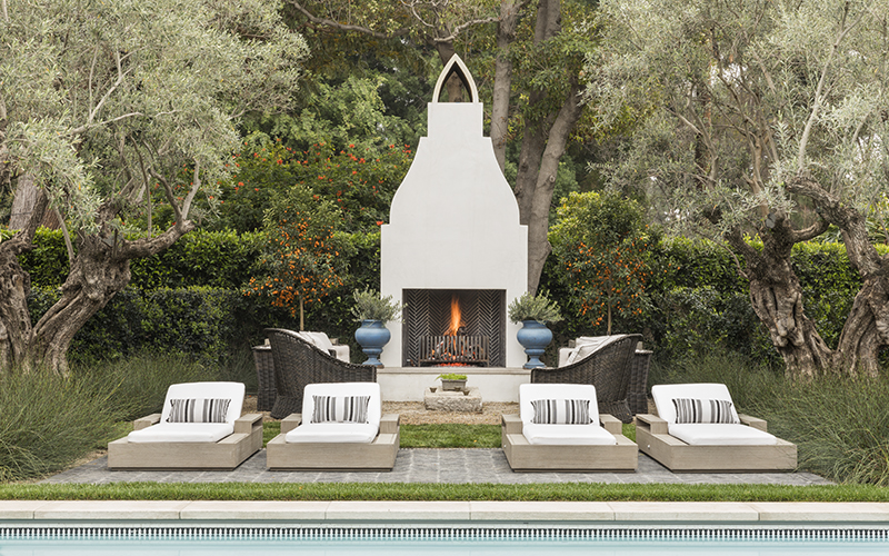 white outdoor fireplace in Moroccan style next to a pool with lounge chairs in front